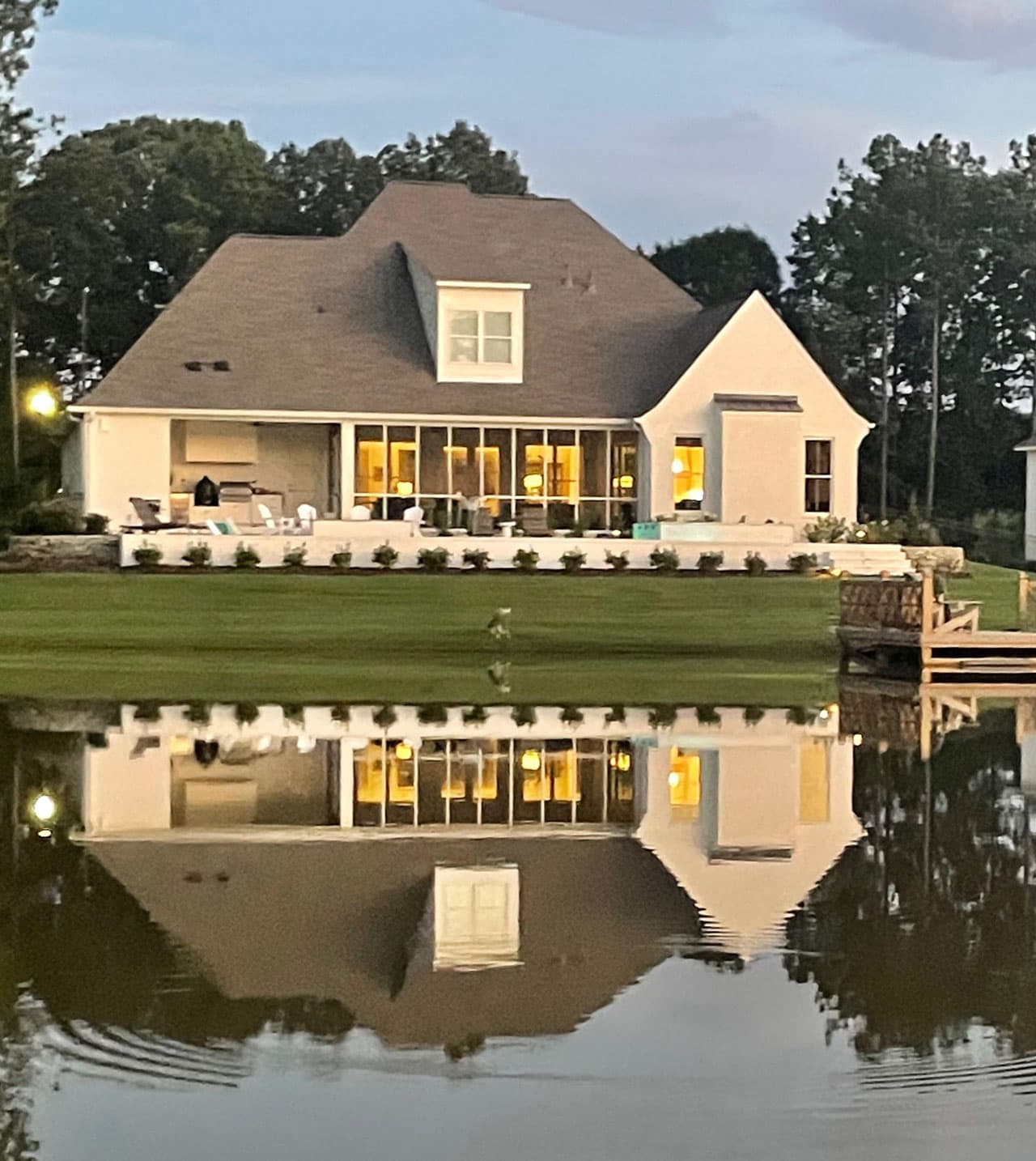A finished house at dusk, lit from inside, mirrored in still water