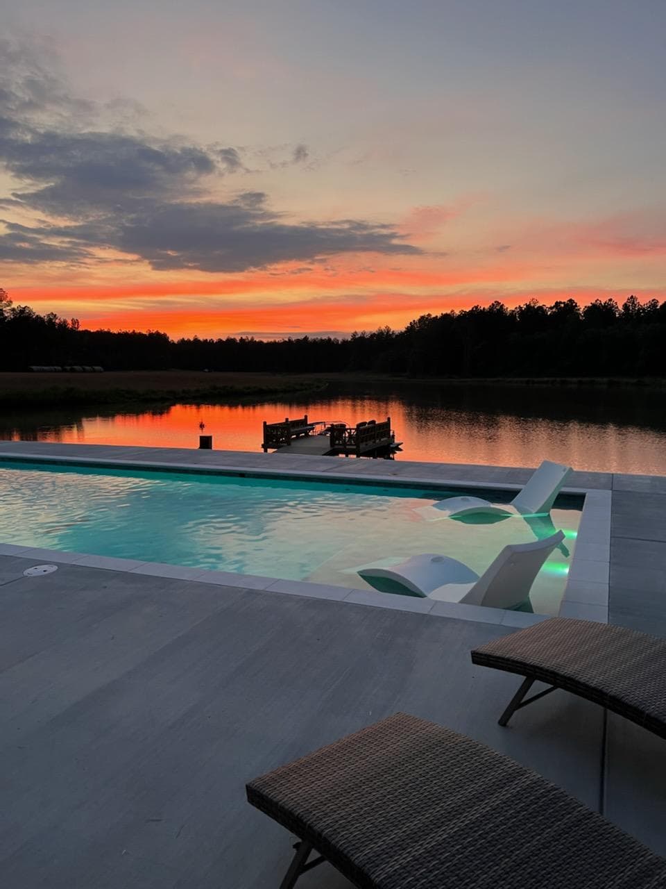 A private pool and loungers at sunset, with a dock on the water beyond